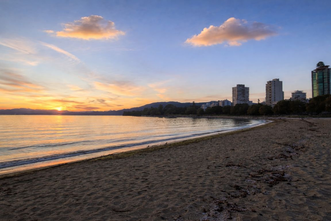 English Bay sandy beach at sunset with calm ocean and Vancouver skyline during a Vancouver Canada Tours excursion